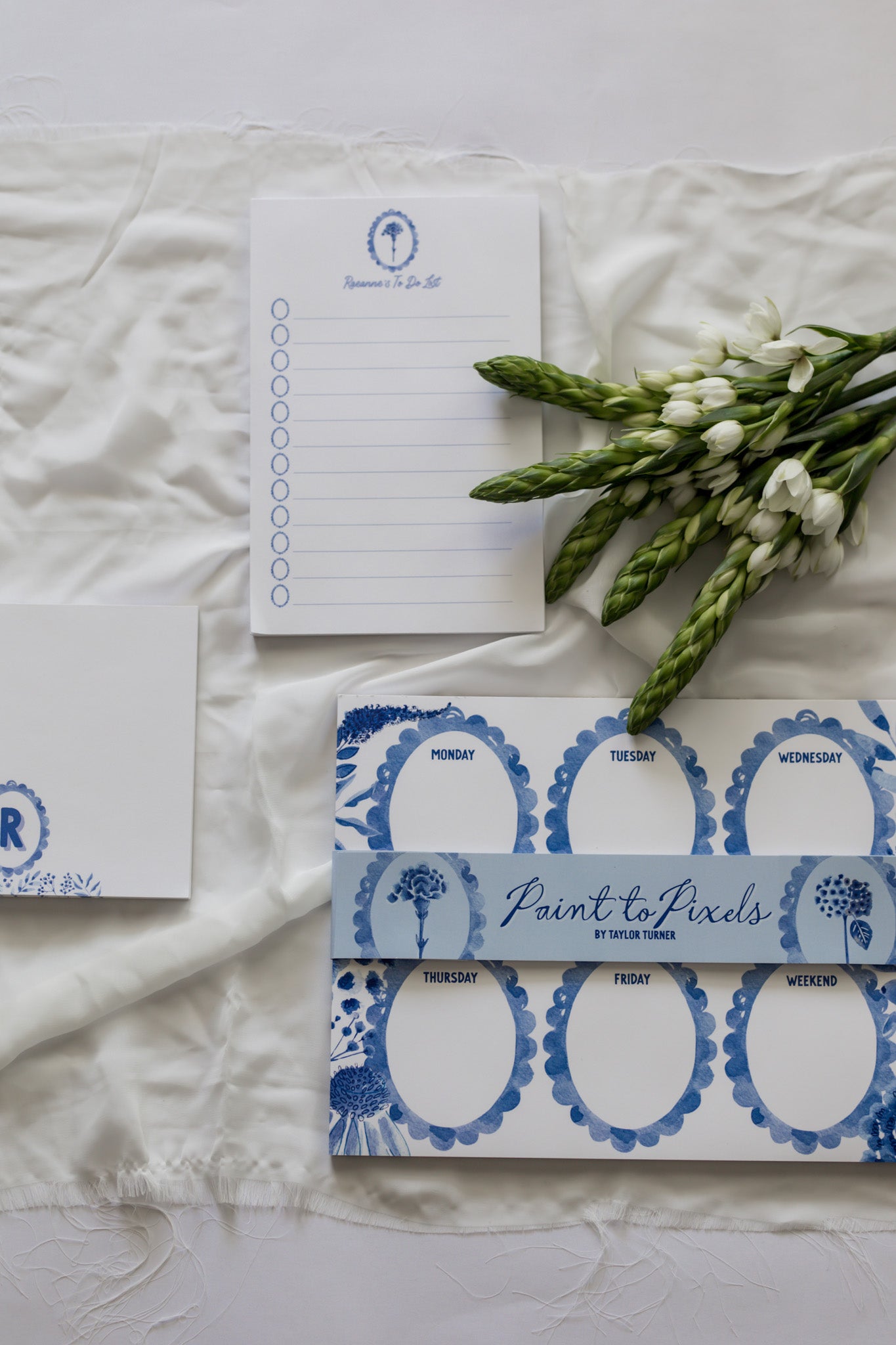 Notebook, stationery items, and flowers on a textured white surface